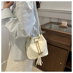 Detail of white drawstring bucket bag with gold chain strap and pearl tassel accessory