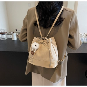 Detail of beige bucket backpack with drawstring closure and cute plush charm