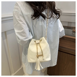 Detail view of white bucket bag featuring drawstring closure, tassel, and pearl pendant