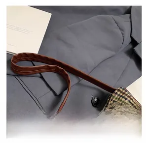 Macro detail of plaid fabric bag showing top opening and leather handle attachment