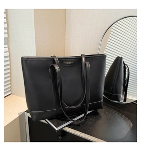 Close-up of a black matte leather tote bag featuring a golden metal logo on a wooden surface