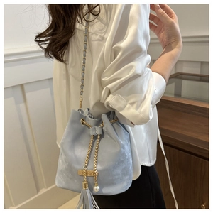 Detail view of light blue bucket bag with gold chain strap, tassels and pearl charm accessory