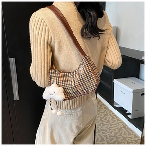 Close-up of houndstooth underarm bag with a white plush cloud charm and leather strap