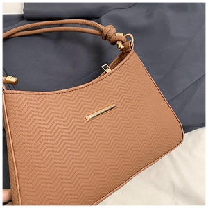 Close-up of caramel leather shoulder bag with wavy texture and gold metal hardware