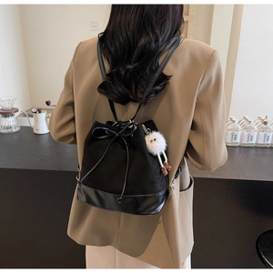 Detail view of black drawstring bucket backpack with plush charm and bow accent
