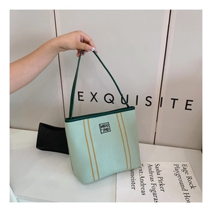 Detail view of mint green canvas bucket bag featuring dark green piping and yellow stripes