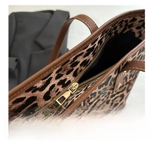 Detailed close-up of smooth golden metal zipper and brown leather trim on leopard tote bag