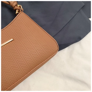 Close-up of caramel leather shoulder bag featuring wavy embossing and gold metal bar