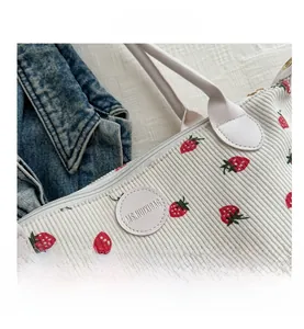 Detail of strawberry print corduroy tote bag with leather logo patch and top zipper