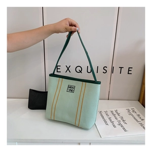 Detailed close-up of light green canvas tote bag with vertical yellow stripes and logo