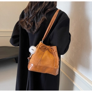 Close-up of brown suede and leather bucket bag with white pompom and drawstring detail