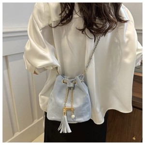 Close-up of light blue velvet bucket bag with gold chain, pearl, and tassel details