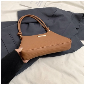 Close-up of caramel shoulder bag with wave pattern texture and gold logo plaque
