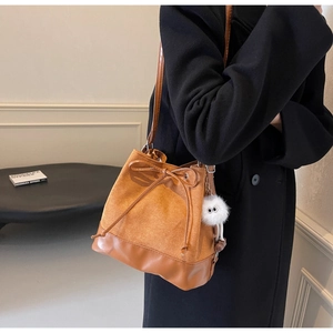 Detail of a brown bucket bag with suede texture, drawstring bow, and a plush monster charm