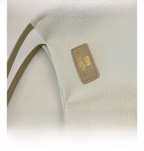 Close-up of textured beige fabric tote bag featuring a leather brand tag and gold lettering
