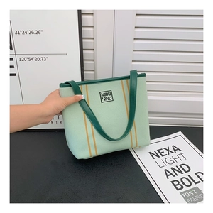 Detail of green canvas tote bag featuring orange ribbons and dark green leather handles