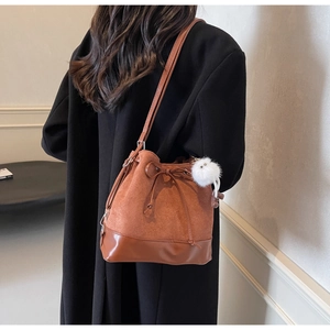 Detail of caramel brown bucket bag featuring a drawstring closure and white pom-pom charm