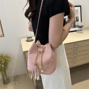 Pink drawstring bucket bag with gold chain strap, tassel and pearl charm in home setting