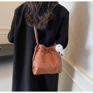 Brown bucket bag detail showing drawstring closure and white plush charm on model