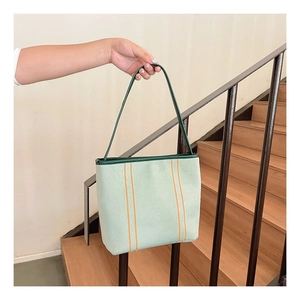 Detail of light green canvas bucket bag featuring orange stripes and green handle straps