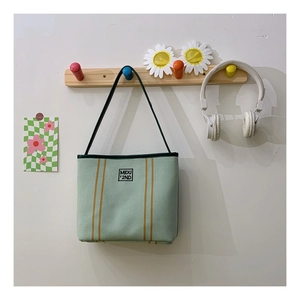 Detail view of a green canvas tote bag with yellow stripes and MIDU logo on a wall hanger