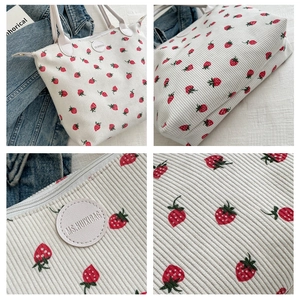 Detail view of strawberry print corduroy tote bag showing metal zipper and brand logo patch