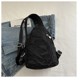 Detail of black nylon sling bag with pleated texture and silver metal zippers