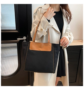 Close-up of black canvas tote with brown leather trim and detailed yellow stitching