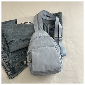 Detail of light blue textured crossbody bag with multiple zippers on denim background