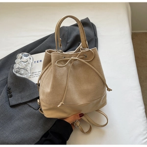 Detail of beige bucket bag with suede texture, drawstring bow, and leather handle