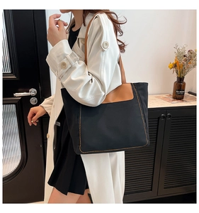 Detail of canvas tote bag showing black fabric with brown leather handles and side stitching
