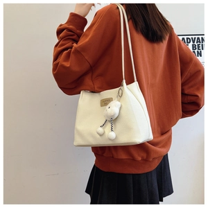 Detail of off-white woven tote bag with a unique plush cloud charm and metal brand plate