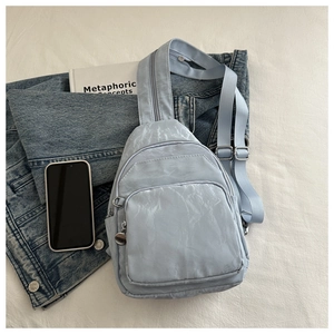 Flat lay of light blue textured nylon chest bag with zip pockets and lifestyle props