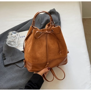 Detail of brown drawstring bucket backpack with suede stitching and silver hardware