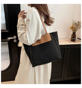 Detail of black canvas tote bag with brown leather flap and yellow contrast stitching