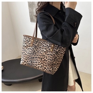 Detail view of leopard print tote bag with brown straps and golden rivets on black coat