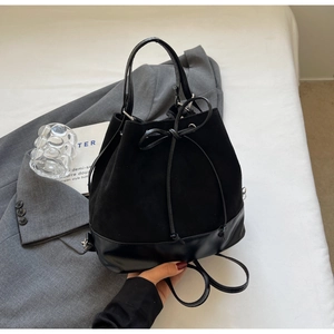 Detail of black drawstring bucket bag with bow accent on a grey suit background