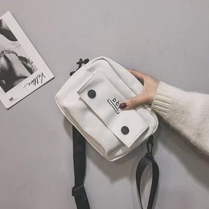 Close-up of a white canvas crossbody bag featuring black adjustable strap and logo detail