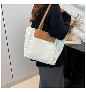 Detail view of large canvas tote bag with brown leather handles and side stitching on model