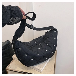 Detailansicht der schwarzen Stepptasche mit bestickten Schleifen und verstellbarem Gurt