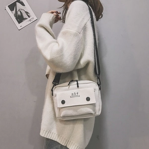 Detail of white canvas crossbody bag featuring DČÝ logo and black shoulder strap
