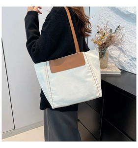 Detail view of large ivory canvas tote bag with brown leather straps worn on shoulder