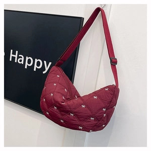 Detail der burgunderroten Stepptasche mit weißer Schleifenstickerei und Gurt