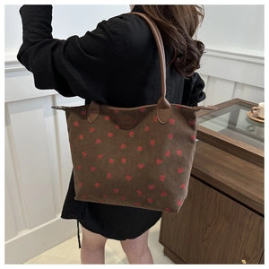 Detail of a brown corduroy tote bag with red strawberry embroidery and leather strap