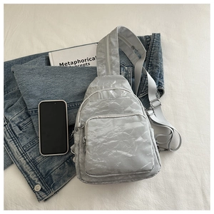 Detail view of light grey textured chest bag with multi-pocket design and wide strap