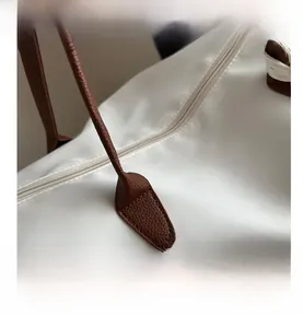 Close-up of the large white tote bag showing brown lychee leather handles and metal zipper
