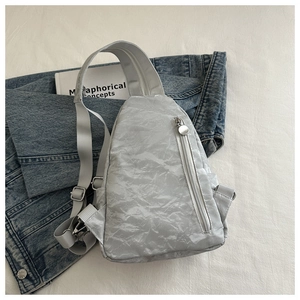 Close-up of light gray crossbody chest bag featuring textured fabric and silver zippers