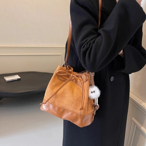 Brown patchwork bucket bag with drawstring bow and plush charm on black coat