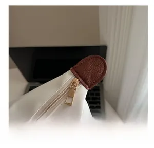 Close-up of smooth champagne gold zipper and brown lychee leather detail on a white tote bag