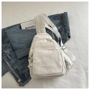 Flat lay of cream nylon sling bag with multi-zipper layers on textured background